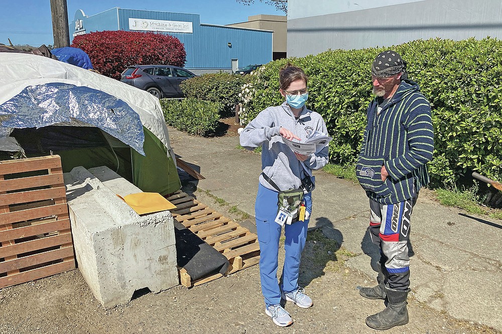 Moira Andrews, a street outreach nurse for Neighborcare Health, speaks with Charles Ussery, 52, who lives in an encampment in the Georgetown neighborhood of Seattle on Monday, April 12, 2021. Andrews spoke with Ussery about the COVID-19 vaccines and answered questions in an effort to vaccinate people experiencing homelessness. Advocates say homeless people are at greater risk of being infected and greater risk of hospitalization and death than the average person, and they should have been prioritized earlier. (AP Photo/Manuel Valdes)