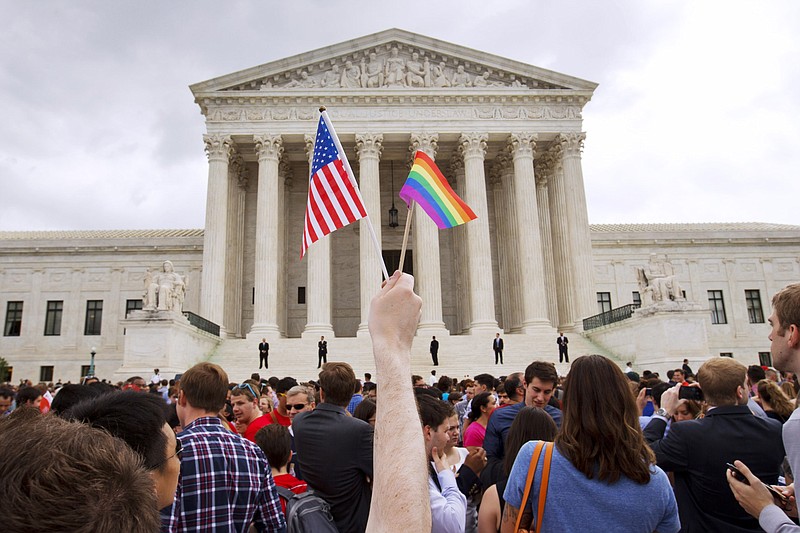 FILE - In this June 26, 2015 file photo, a man holds a U.S. and a rainbow flag outside the Supreme Court in Washington after the court legalized gay marriage nationwide. Court documents show the state of Alaska for years maintains a discriminatory policy that denied some same-sex spouses benefits by wrongly claiming gay marriage was not recognized in Alaska, long after courts ordered they be recognized. (AP Photo/Jacquelyn Martin, File)