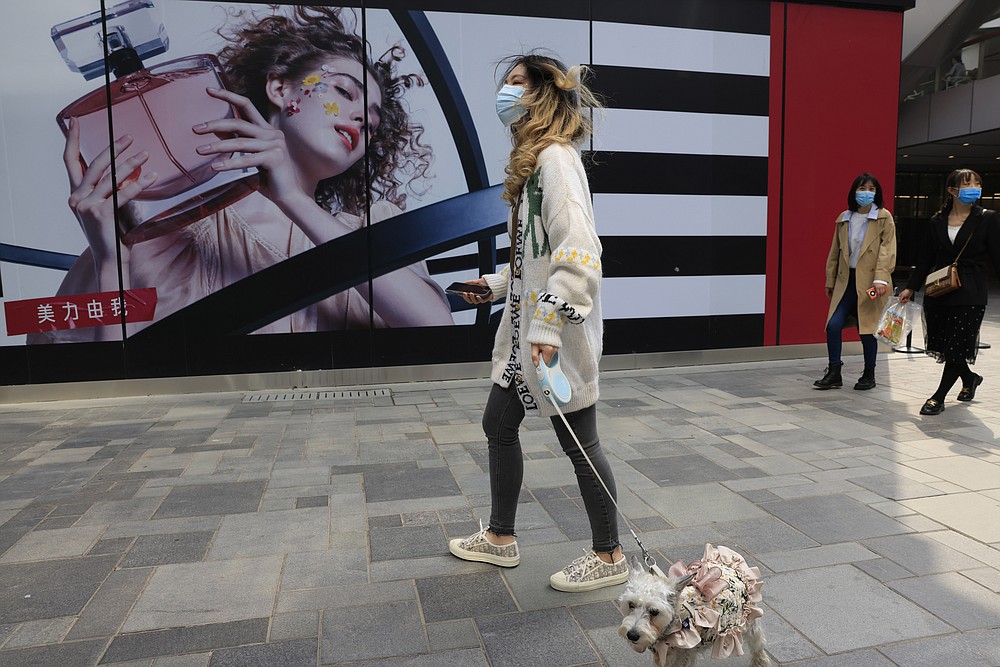 Een vrouw laat haar hond uit in een winkelgebied in Peking op donderdag 15 april 2021. De Chinese economische groei steeg in het eerste kwartaal van dit jaar naar 18,3% jaar-op-jaar toen de fabrieks- en consumentenactiviteit herstelde van de coronaviruspandemie.  (AP Photo / Ng Han Guan)