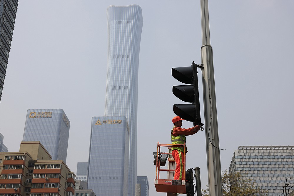 Een werknemer installeert op donderdag 15 april 2021 nieuwe verkeerslichten op een kruispunt in Peking. De Chinese economische groei steeg in het eerste kwartaal van dit jaar naar 18,3% toen de fabrieks- en consumentenactiviteit herstelde van de coronaviruspandemie.  (AP Photo / Ng Han Guan)