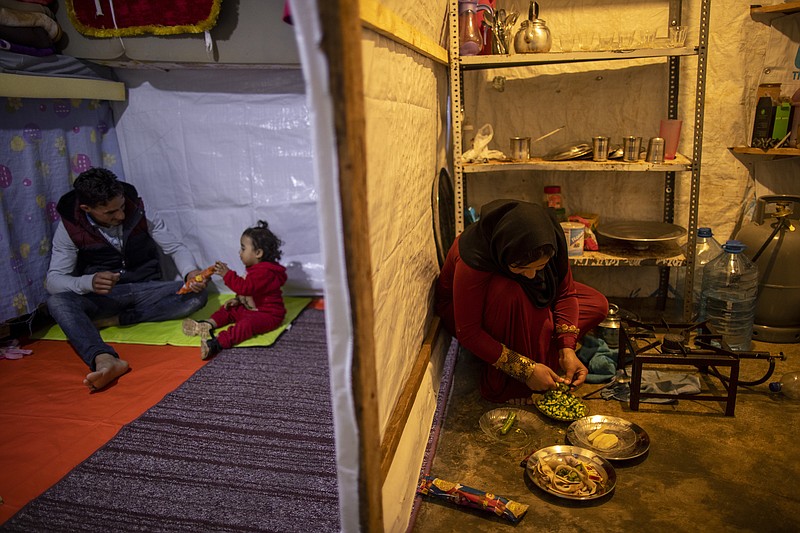 Syrian refugee Ayesha al-Abed, 21, right, prepares food as her Husband Raed Mattar, 24, left, plays with their daughter Rayan, 18 months old, before they break their fast on the first day of fasting month of Ramadan, at an informal refugee camp, in the town of Bhannine in the northern city of Tripoli, Lebanon, Tuesday, April 13, 2021. For many Syrian refugee families in Lebanon, Ramadan comes as a hard life of displacement has gotten even harder after a pandemic year that deepened economic woes in their host country. (AP Photo/Hassan Ammar)