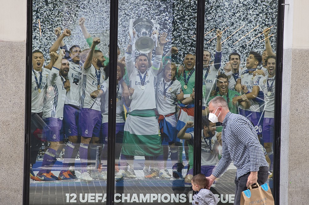 A man and a young boy walk past a Real Madrid poster of the team celebrating in a merchandising shop in Madrid, Spain, Monday, April 19, 2021. UEFA president Aleksander Ceferin says players at the 12 clubs setting up their own Super League could be banned from this year's European Championship and next year's World Cup. Ceferin spoke after a UEFA executive committee meeting held only hours of the English, Italian and Spanish clubs announced the project that threatens to split European soccer. (AP Photo/Paul White)