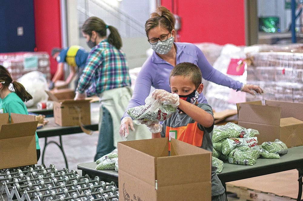 Phoenix resident Erin Pfeifer, 40, unloads boxes of bagged peas as her 8-year-old son, Dylan, places them into the boxes at St. Mary's Food Bank in Phoenix on Thursday, March 18, 2021. This was the second volunteer event Pfeifer and her son attended with the food bank. (AP Photo/Cheyanne Mumphrey)