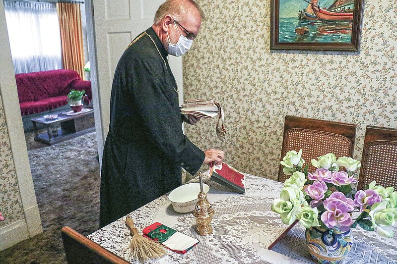 Father Mark Elliott, of St. George Greek Orthodox Church arranges items before starting a house blessing at Kathleen Chamis' residence  Tuesday, March 9, 2021 in Ashland, Ky. After more than a year of fighting an ongoing pandemic, most are ready for a cleansing and Father Mark Elliott of St. George Greek Orthodox Church in Huntington is trying to bring them some peace. (Matt Jones/The Daily Independent via AP)