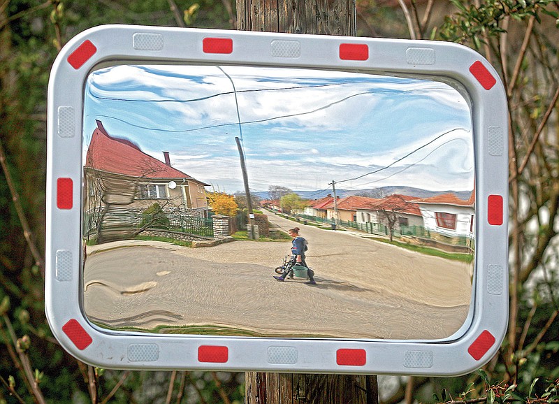 Karmen Bastyur, a 22 year old Hungarian Roma woman, is reflected in a traffic mirror carrying a bucket of drinking water from a public water pump in Bodvaszilas, Hungary, Monday, April 12,2021. TMany students from Hungary's Roma minority do not have access to computers or the internet and are struggling to keep up with online education during the pandemic. Surveys show that less than half of Roma families in Hungary have cable and mobile internet and 13% have no internet at all. (AP Photo/Laszlo Balogh)