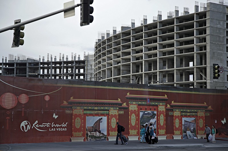 FILE - In this May 16, 2017, file photo, people walk by the Resorts World Las Vegas site in Las Vegas. On Monday, April 19, 2021, Resorts World Las Vegas announced that it will open June 24, and began taking reservations for more than 3,500 rooms at its three Hilton-branded hotels. (AP Photo/John Locher, File)