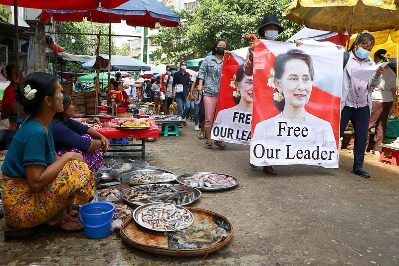 FILE - In this April 8, 2021, file photo, anti-coup protesters walk through a market with images of ousted Myanmar leader Aung San Suu Kyi in Yangon, Myanmar. Aid workers and activists are warning Myanmar's political upheavals could cause a regional refugee crisis as political strife following a Feb. 1 coup displace growing numbers of people who have lost their livelihoods. coming in a couple hours. (AP Photo, File)