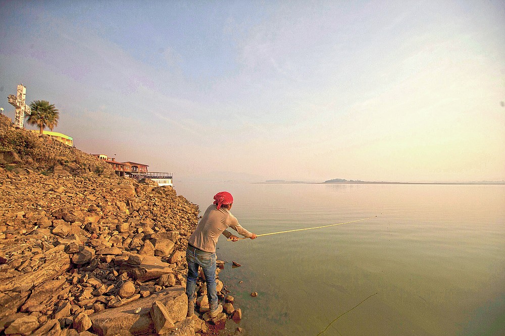 A man fishes off the banks of the Villa Victoria Dam, the main water supply for Mexico City residents, on the outskirts of Toluca, Mexico Thursday, April 22, 2021. Drought conditions now cover 85% of Mexico, and in areas around Mexico City and Michoacán, the problem has gotten so bad that lakes and reservoirs are drying up. (AP Photo/Fernando Llano)