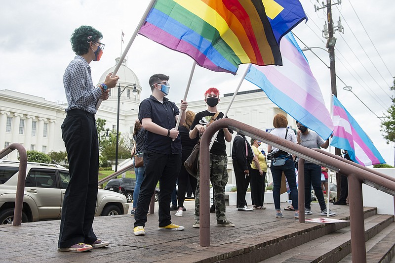 FILE - In this Tuesday, March 30, 2021 file photo, demonstrators in support of transgender rights hold flags during a rally outside the Alabama State House in Montgomery, Ala.  Five states have passed laws or implemented executive orders this year limiting the ability of transgender youths to play sports or receive certain medical treatment. There’s been a vehement outcry from supporters of transgender rights – but little in the way of tangible repercussions for those states. (Jake Crandall/The Montgomery Advertiser via AP)