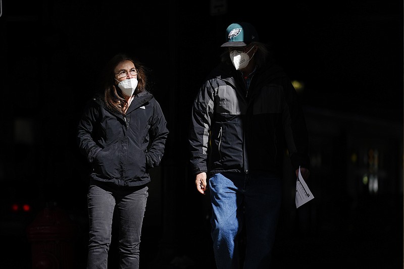 FILE - In this Wednesday, March 3, 2021 file photo, people wearing face masks as a precaution against the coronavirus walk through a shaft of light on a street in Philadelphia. On Tuesday, April 27, 2021, U.S. health officials say fully vaccinated Americans don't need to wear masks outdoors anymore unless they are in a big crowd of strangers, and those who are unvaccinated can go without a face covering outside in some cases, too. (AP Photo/Matt Rourke)