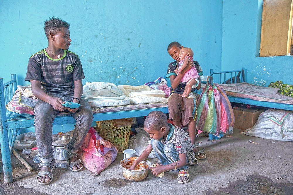 Tigrayan 11-year-old refugee Daniel Gebremariam holds his 4-month-old sister, Turfu, as his 5-year-old brother, Micheale, eats with their 19-year-old uncle, Goytom Tsegay, left, inside the family's shelter in Hamdayet, eastern Sudan, near the border with Ethiopia, on March 21, 2021. (AP Photo/Nariman El-Mofty)