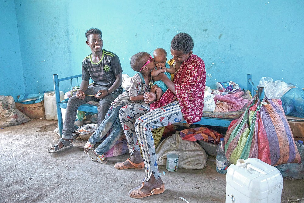 Tigrayan 5-year-old refugee Micheale Gebremariam kisses his 4-month-old sister, Aden, as his 19-year-old uncle, Goytom Tsegay, left, sits with them, inside their family's shelter in Hamdayet, eastern Sudan, near the border with Ethiopia, on March 21, 2021. (AP Photo/Nariman El-Mofty)