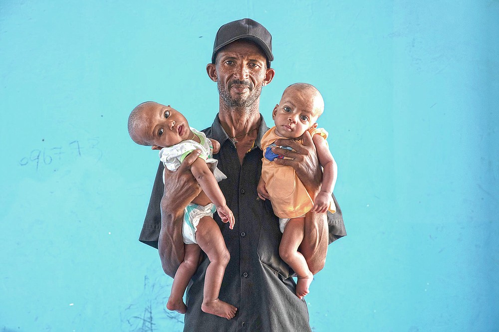 Tigrayan refugee Abraha Kinfe Gebremariam, 40, holds his 4-month-old twin daughters Aden, left, and Turfu, inside their family's shelter in Hamdayet, eastern Sudan, near the border with Ethiopia, on March 23, 2021. Abraha searches their faces for traces of their mother. Babies change, especially this young, he says. But for now, his family agrees, one of the girls does look like Letay. (AP Photo/Nariman El-Mofty)