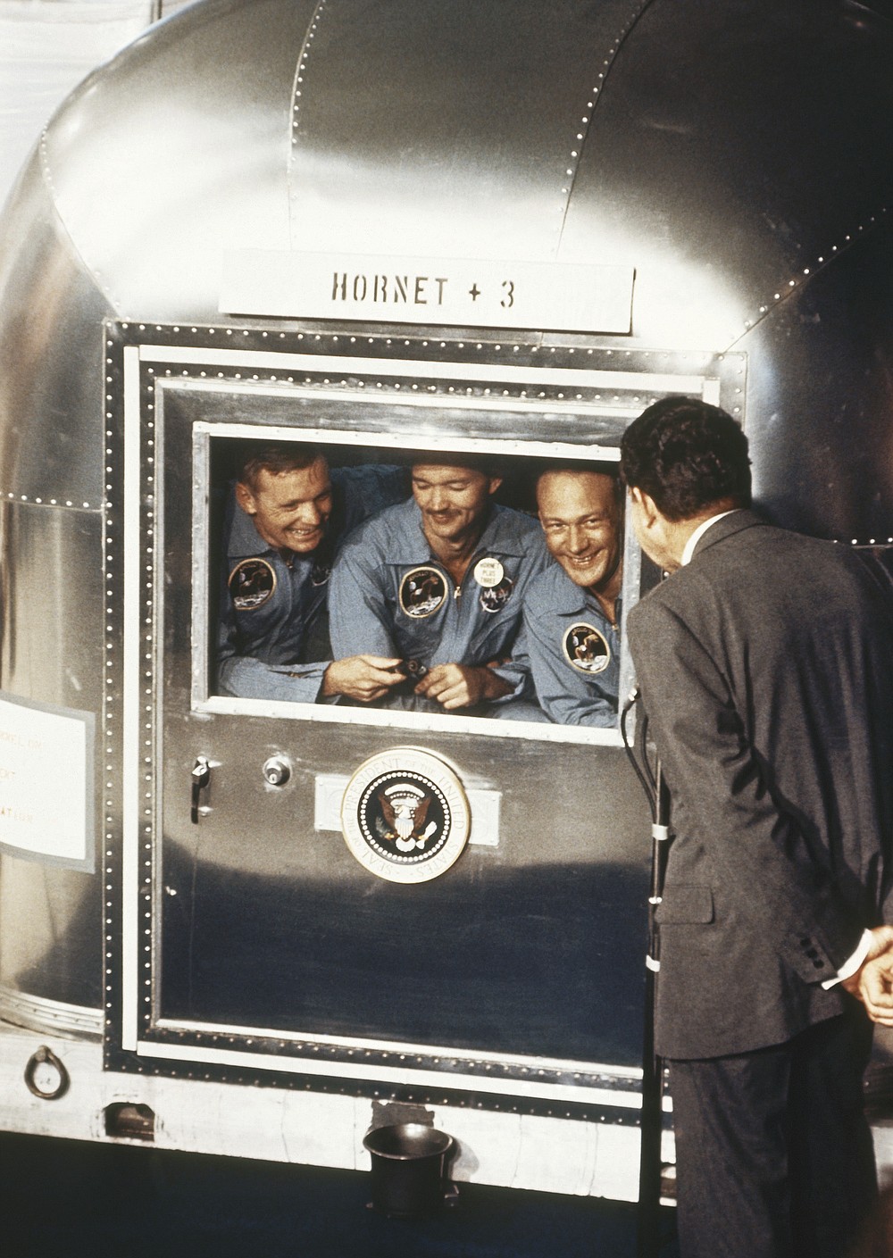 FILE - In this July 24, 1969 file photo, President Richard Nixon, back to camera, greets the Apollo 11 astronauts in a quarantine van on board the U.S.S. Hornet after splashdown and recovery in the Pacific Ocean. From left are Neil Armstrong, Michael Collins, and Edwin "Buzz" Aldrin. Splashdown was east of Wake Island, and south of Johnston Atoll. Collins, who piloted the ship from which Armstrong and Aldrin left to make their historic first steps on the moon in 1969, died Wednesday, April 28, 2021, of cancer, his family said. He was 90. (AP Photo/File)
