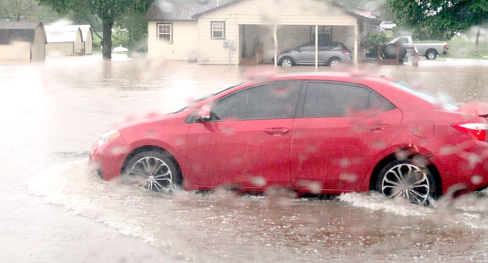 Marc Hayot/Siloam Sunday A car navigates the flooded parking lot of the county and state offices on South Lincoln Street on Wednesday. The flooding was caused by excessive rain that came to Siloam Springs that day.