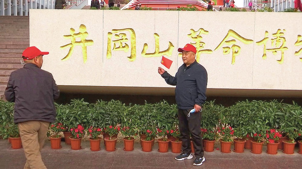 A tourist holds a flag as he poses for photos in front of the sign for the Jinggangshan Revolution Museum in Jinggangshan, southeast China's Jiangxi Province, on April 8, 2021.  For the centenary of the Chinese Communist Party, tourists flock to China's historical sites and pilgrimages to party landmarks.  (AP Photo / Emily Wang)
