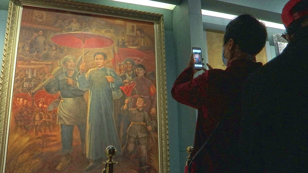 A tourist takes photos of a painting depicting the late Communist leader Mao Zedong, at the Jinggangshan Revolution Museum in Jinggangshan in southeastern China's Jiangxi province, on April 8, 2021. On the hundredth anniversary of the Chinese Communist Party, tourists in China are flocking to historic sites and making pilgrimages to party landmarks. (AP Photo/Emily Wang)