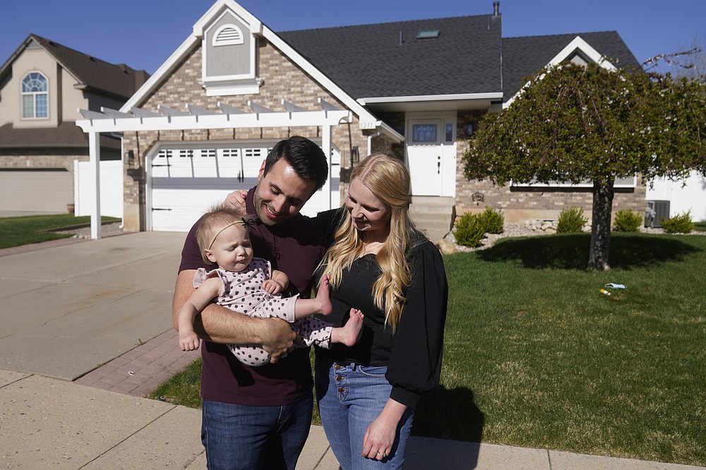 FILE - Matthew Clewett, 26, holds his daughter Nellie, while his wife Bethany looks on at their home Thursday, April 29, 2021, in Kaysville, Utah. Utah is one of two Western states known for rugged landscapes and wide-open spaces that are bucking the trend of sluggish U.S. population growth. The Clewett's want to have a large family like the ones they grew up in, but high housing costs could put a serious damper on that plan. The couple bid on at least 10 houses in northern Utah before they could close on a starter home for themselves and their infant daughter. (AP Photo/Rick Bowmer)
