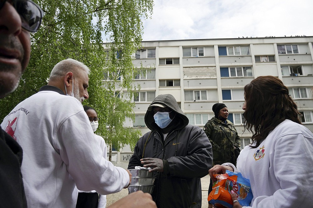 Founder of 'Laissez Les Servir' (Let Them Serve) Nourouddine Abdoulhoussen, left, and member Mina distribute food in the Fauvettes projects, Pierrefitte-sur-Seine, north of Paris, Thursday, April 29, 2021. Nourouddine Abdoulhoussen, a former member of the 8th Marine Infantry Parachute Regiment, runs a tight ship, reaching into his years in the military to inculcate in his proteges, youths from poor French suburbs, confidence, courage and love of France. To the youth in (Let Them Serve) the white-bearded 53-year-old leader with the booming voice is “the Captain.” (AP Photo/Thibault Camus)