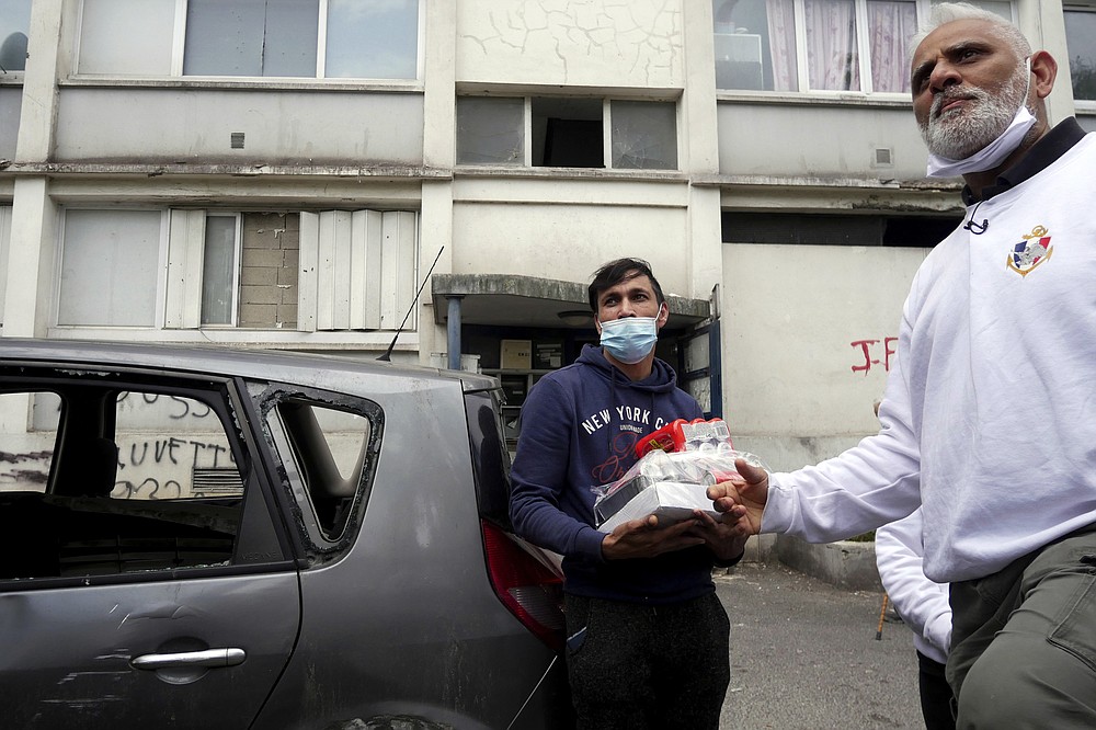 A member of 'Laissez Les Servir' (Let Them Serve) distributes food in the Fauvettes projects, Pierrefitte-sur-Seine, north of Paris, Thursday, April 29, 2021. Nourouddine Abdoulhoussen, a former member of the 8th Marine Infantry Parachute Regiment, runs a tight ship, reaching into his years in the military to inculcate in his proteges, youths from poor French suburbs, confidence, courage and love of France. To the youth in (Let Them Serve) the white-bearded 53-year-old leader with the booming voice is “the Captain.” (AP Photo/Thibault Camus)