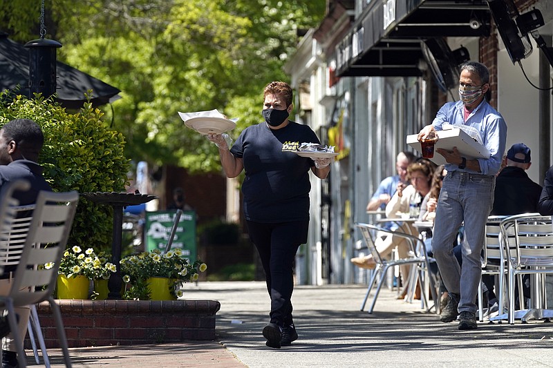 A member of the wait staff takes food to outdoor diners at the Mediterranean Deli restaurant in Chapel Hill, N.C., Friday, April 16, 2021. Thousands of restaurants and bars decimated by COVID-19 have a better chance at survival as the government begins handing out $28.6 billion in grants _ money to help these businesses stay afloat while they wait for customers to return. The Small Business Administration is accepting applications for grants from the Restaurant Revitalization Fund as of Monday, May 3. (AP Photo/Gerry Broome)