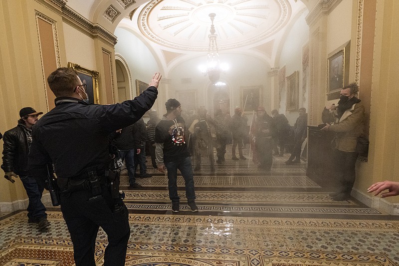 FILE - In this Jan. 6, 2021, file photo, smoke fills the walkway outside the Senate Chamber as supporters of President Donald Trump are confronted by U.S. Capitol Police officers inside the Capitol in Washington. With riot cases flooding into Washington’s federal court, the Justice Department is under pressure to quickly resolve the least serious cases. (AP Photo/Manuel Balce Ceneta, File)