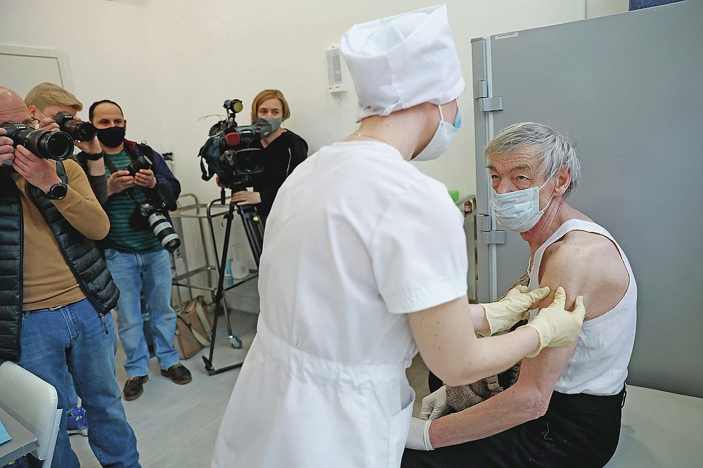 An elderly man wearing a face mask to protect against coronavirus receives a shot of Russia's Sputnik V coronavirus vaccine in front of working visual journalists at a vaccination point in Moscow, Russia, Wednesday, April 7, 2021. To boost the demand, officials in Moscow this week started offering 1,000-ruble ($13) coupons to people over 60 for getting vaccinated. So far, the incentive hasn't elicited a lot of enthusiasm among elderly Muscovites. (AP Photo/Pavel Golovkin)