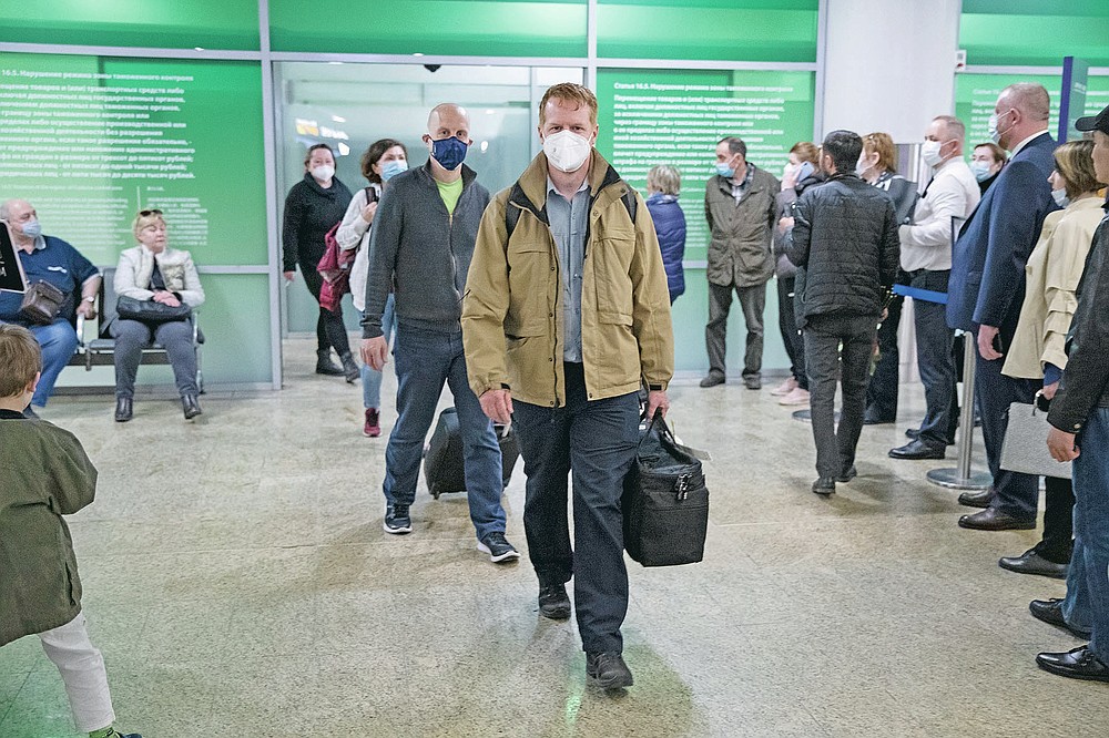 Germany's Enno Lenze, center, and Uwe Keim, center left, both wearing face masks to protect agains coronavirus, enter the hall after arriving at Sheremetyevo airport, outside Moscow, Russia, Thursday, April 15, 2021. The abundance of vaccines in the Russian capital has been drawing in vaccine tourists, not just from other regions, where the wait for a shot is longer, but foreigners, too. A group of Germans traveled to Moscow earlier this month and got their first shots right at their hotel. (AP Photo/Pavel Golovkin)