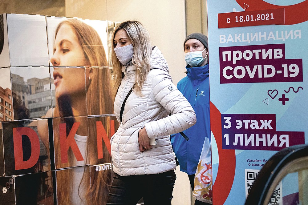 A woman wearing a face mask to protect against coronavirus walks past a poster reading "vaccination against COVID-19" at the GUM, the State Department store, near Red Square in Moscow, Russia, Wednesday, March 31, 2021. Russia has boasted about being the first country in the world to authorize a coronavirus vaccine and rushed to roll it out earlier than other countries, even as large-scale testing necessary to ensure its safety and effectiveness was still ongoing. (AP Photo/Alexander Zemlianichenko)