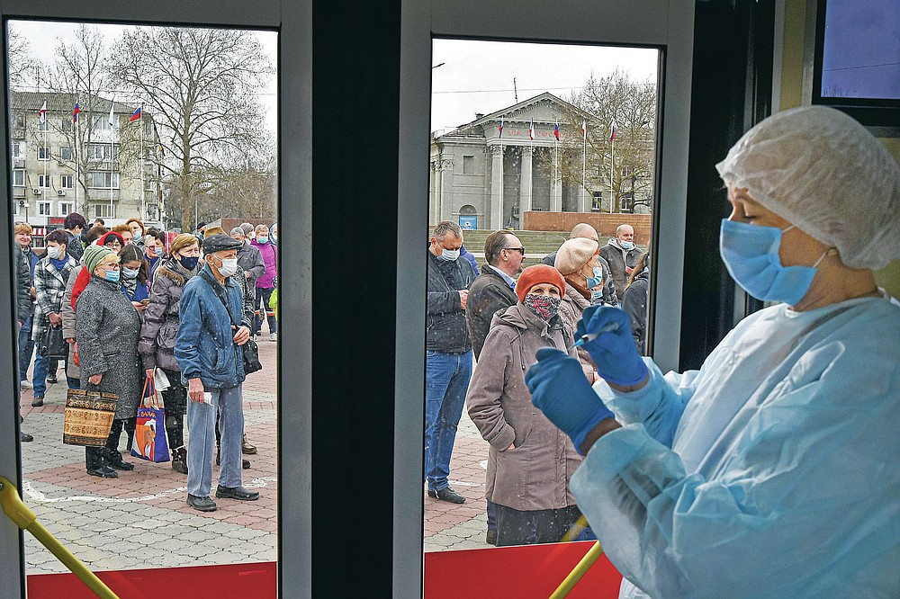 A Russian medical worker prepares a shot of Russia's Sputnik V coronavirus vaccine as people wearing face masks to protect against coronavirus queue to get a shot of Russia's Sputnik V coronavirus vaccine in a mobile vaccination center in Simferopol, Crimea, Tuesday, April 13, 2021. Alexander Dragan, a data analyst who has been tracking vaccination in the Russian regions, says Russia is currently vaccinating 200,000-205,000 people a day. In order to immunize 30 million people by mid-June, it needs to be nearly double that: "We need to start vaccinating 370,000 people a day, like, beginning tomorrow," Dragan told the AP. (AP Photo/Alexander Polegenko)