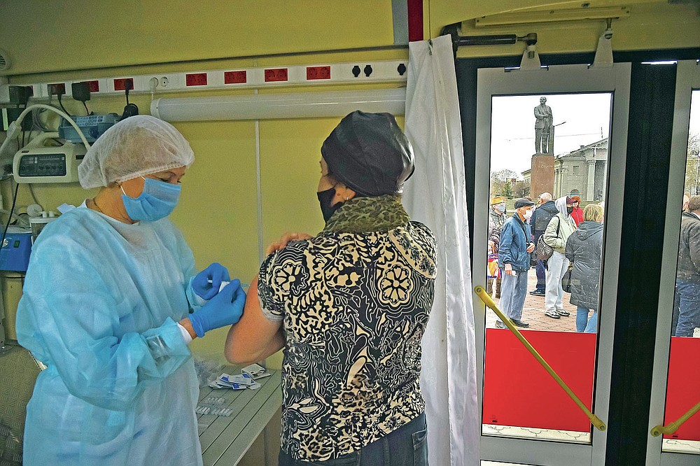A Russian medical worker administers a shot of Russia's Sputnik V coronavirus vaccine for a woman as people wearing face masks to protect against coronavirus queue to get a shot of Russia's Sputnik V coronavirus vaccine in a mobile vaccination center with a statue of Vladimir Lenin in the background in Simferopol, Crimea, Tuesday, April 13, 2021. Russia has boasted about being the first country in the world to authorize a coronavirus vaccine and rushed to roll it out earlier than other countries, even as large-scale testing necessary to ensure its safety and effectiveness was still ongoing. (AP Photo/Alexander Polegenko)