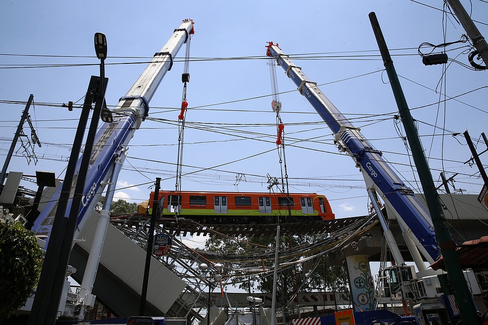 A subway car is prepared to be lowered to the ground, with the help of cranes, from a collapsed elevated section of the metro, in Mexico City, Tuesday, May 4, 2021. The elevated section of the Line 12 metro collapsed late Monday, killing at least 23 people and injuring at least 79, city officials said. (AP Photo/Marco Ugarte)