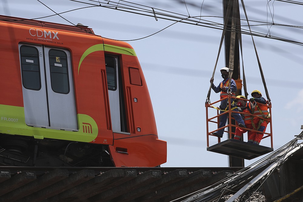 A subway car is prepared to be lowered to the ground, with the help of a crane, from a collapsed elevated section of the metro, in Mexico City, Tuesday, May 4, 2021. The elevated section of the Line 12 metro collapsed late Monday, killing at least 23 people and injuring at least 79, city officials said. (AP Photo/Marco Ugarte)
