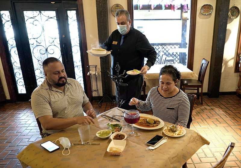 FILE - In this Wednesday, March 10, 2021 file photo, waiter Jose Bravo, center, delivers food for Alberto Castaneda, left, and his wife, Esther, at Picos restaurant in Houston. The Institute for Supply Management, an association of purchasing managers, reported Monday, April 5 that the U.S. services sector, which employs most Americans, recorded record growth in March as orders, hiring and prices all surged.  (AP Photo/David J. Phillip, File)