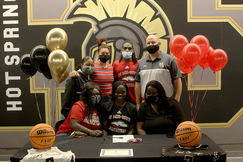 Hot Springs’ Jaylia Reed, seated center, smiles after signing a letter of intent to play basketball at Arkansas State University Mid-South during a ceremony at Trojan Arena Friday. Reed was joined by, seated from left, sister Anaya Reed, mother Jeremy Burns, standing from left, Lady Trojans assistant coach Nicole Lowe, friend Jurnee Hicks, brother Leshawn Reed and Lady Trojans head coach Josh Smith. - Photo by James Leigh of The Sentinel-Record