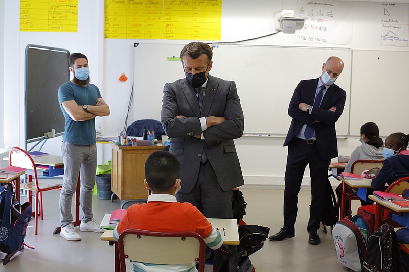 FILE - In this April, 26, 2021 file photo, French President Emmanuel Macron talks with a pupil during a visit with French Education, Youth and Sports Minister Jean-Michel Blanquer, right, in a school in Melun, south of Paris. The ministry of education this week banned the use in schools of an increasingly widespread method to make French more inclusive by feminizing some words. (AP Photo/Thibault Camus, File)