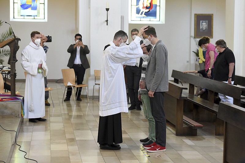 Vicar Wolfgang Rothe, center, blesses two men during a Catholic service with the blessing of same-sex couples in St Benedict's Church in Munich, Sunday, May 9, 2021. Germany’s Catholic progressives are openly defying a recent Holy See pronouncement that priests cannot bless same-sex unions by offering exactly such blessings at services in about 100 different churches all over the country. The blessings at open worship services are the latest pushback from German Catholics against a document released in March by the Vatican’s orthodoxy office, which said Catholic clergy cannot bless same-sex unions. (Felix Hoerhager/dpa via AP)
