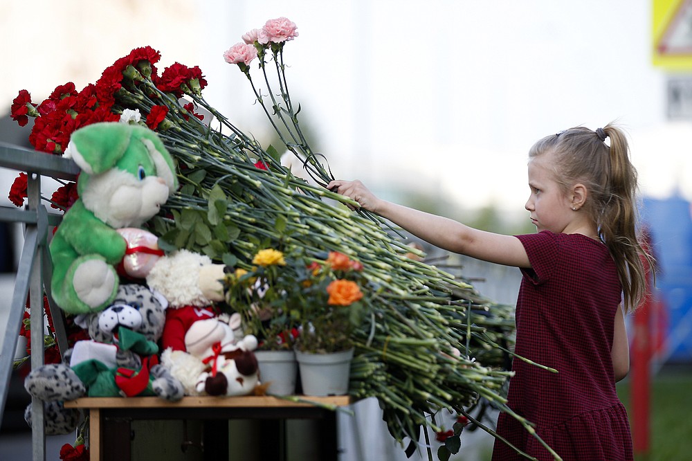 A girl lays flowers near a school after a shooting in Kazan, Russia, Tuesday, May 11, 2021. Russian officials say a gunman attacked a school in the city of Kazan and Russian officials say several people have been killed. Officials said the dead in Tuesday's shooting include students, a teacher and a school worker. Authorities also say over 20 others have been hospitalized with wounds. (AP Photo/Roman Kruchinin)