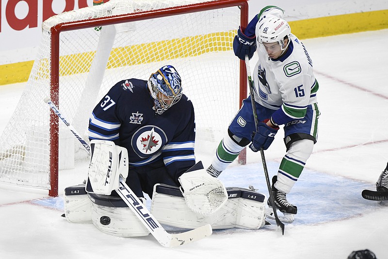 Winnipeg Jets' goaltender Connor Hellebuyck (37) makes a save on a Vancouver Canucks shot as Matthew Highmore (15) looks for the rebound during the second period of Tuesday's game in Winnipeg, Manitoba. - Photo by Fred Greenslade/The Canadian Press via The Associated Press