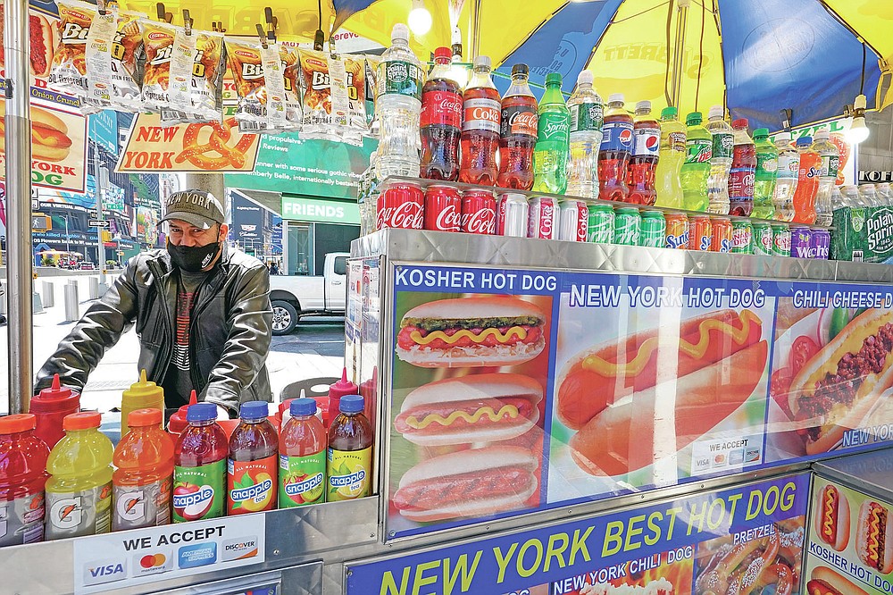 Mohammed Hussein works at his hot dog vending cart in New York's Times Square, Tuesday, April 27, 2021. In recent weeks, tourism indicators for New York City like hotel occupancy and museum attendance that had fallen off a pandemic cliff have ticked up slightly. It's a welcome sight for a city where the industry has been decimated by the impact of the coronavirus. (AP Photo/Mary Altaffer)