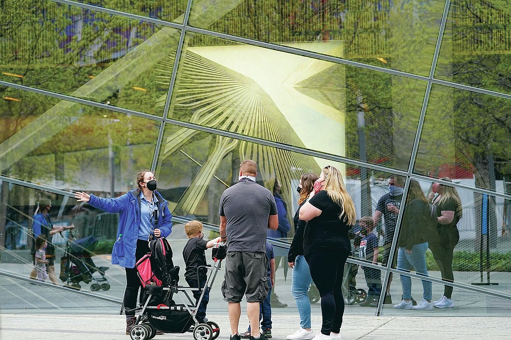 A 9/11 Memorial & Museum Visitor Services associate, left, gives visitors information and directions, Thursday, April 29, 2021, in New York. In recent weeks, tourism indicators for New York City like hotel occupancy and museum attendance that had fallen off a pandemic cliff have ticked up slightly. It's a welcome sight for a city where the industry has been decimated by the impact of the coronavirus. (AP Photo/Mary Altaffer)