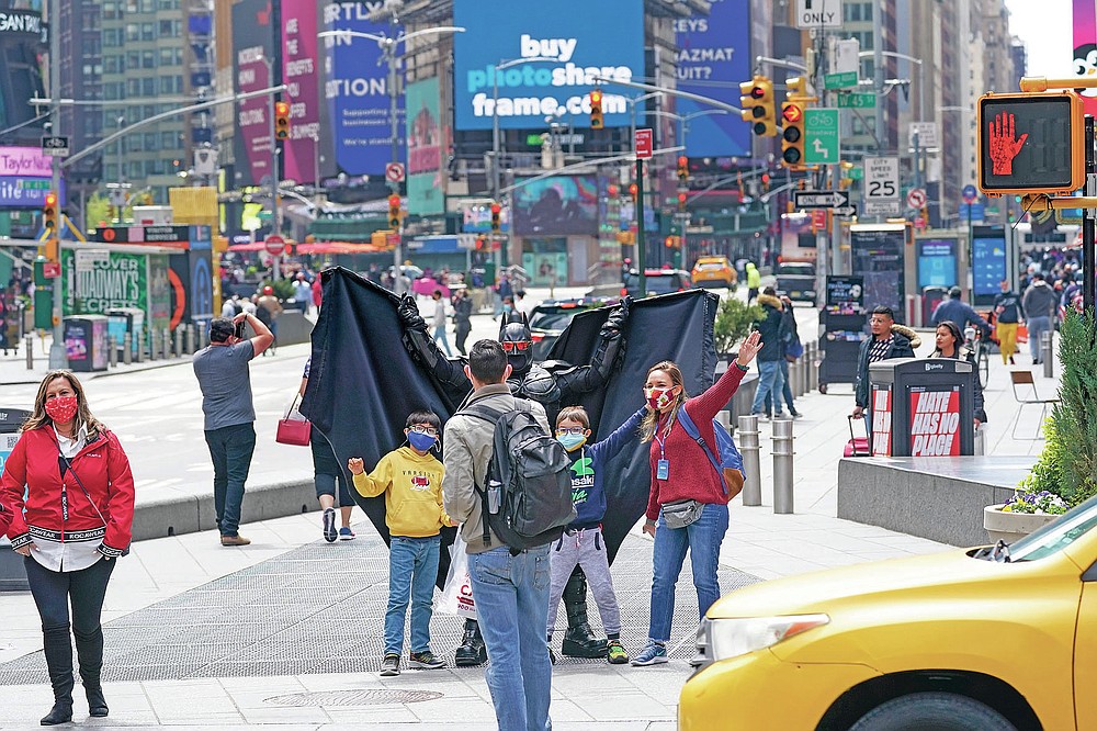 Visitors to New York's Time Square pose for a photo with a street performer working for tips dressed as Batman, Tuesday, April 27, 2021. In recent weeks, tourism indicators for New York City like hotel occupancy and museum attendance that had fallen off a pandemic cliff have ticked up slightly. It's a welcome sight for a city where the industry has been decimated by the impact of the coronavirus. (AP Photo/Mary Altaffer)