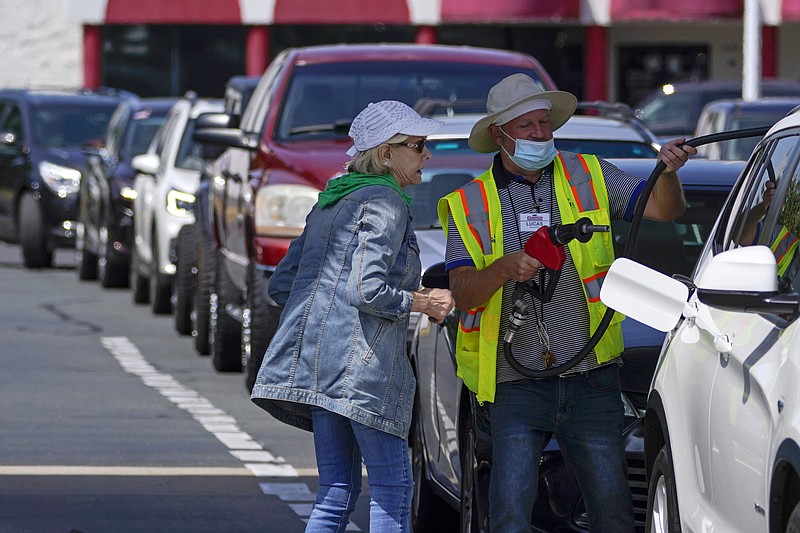 A customer helps pumping gas at Costco, as other wait in line, on Tuesday, May 11, 2021, in Charlotte, N.C. Colonial Pipeline, which delivers about 45% of the fuel consumed on the East Coast, halted operations last week after revealing a cyberattack that it said had affected some of its systems. (AP Photo/Chris Carlson)