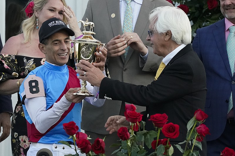 Trainer Bob Baffert hands the winner's trophy to jockey John Velazquez after they victory with Medina Spirit in the 147th running of the Kentucky Derby at Churchill Downs, Saturday, May 1, 2021, in Louisville, Ky. (AP Photo/Jeff Roberson)
