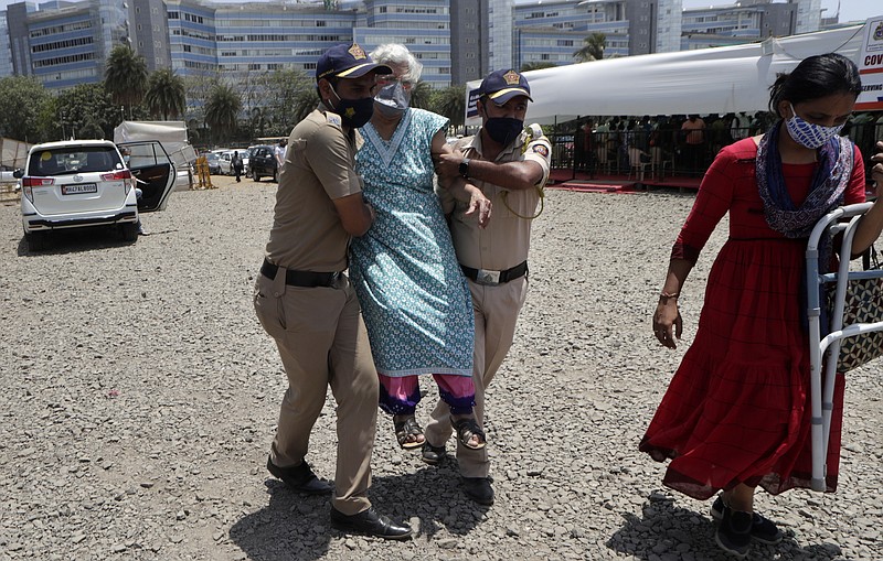 FILE- In this April 24, 2021, file photo, police personnel help an elderly woman outside a vaccination center in Mumbai, India. Misinformation about the coronavirus is surging in India as the death toll from COVID-19 rises. Fueled by anguish, distrust and political polarization, the claims are further compounding India's crisis. (AP Photo/Rajanish Kakade, File)