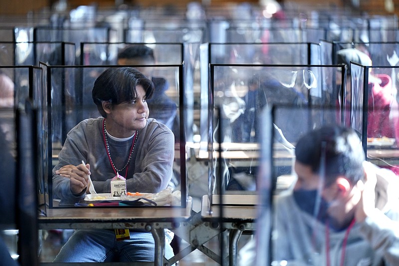 FILE - In this March 21, 2021, file photo, students sit separated by plastic dividers during lunch at Wyandotte County High School in Kansas City, Kan., on the first day of in-person learning. Children are having their noses swabbed or saliva sampled at school to test for the coronavirus in cities. As more children return to school buildings this spring, widely varying approaches have emerged on how and whether to test students and staff members for the virus. (AP Photo/Charlie Riedel, File)