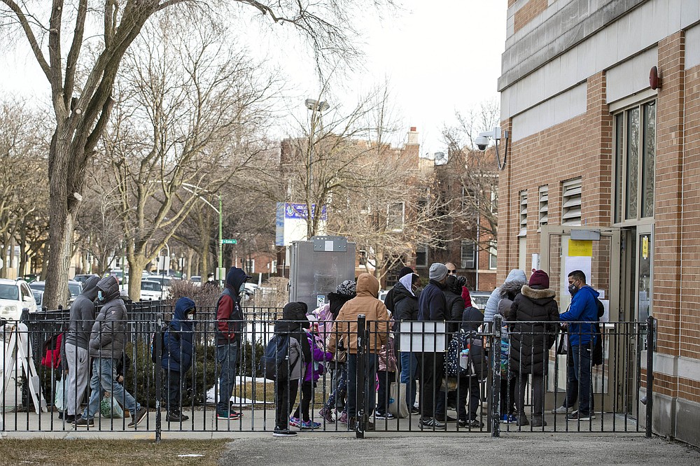 FILE - In this March 1, 2021, file photo, parents and children line up outside George B. Armstrong International Studies Elementary School, as students return to in-person learning at the Rogers Park neighborhood school on the North Side of Chicago. Children are having their noses swabbed or saliva sampled at school to test for the coronavirus in cities such as Baltimore, New York and Chicago. As more children return to school buildings this spring, widely varying approaches have emerged on how and whether to test students and staff members for the virus. (Ashlee Rezin Garcia/Chicago Sun-Times via AP, File)