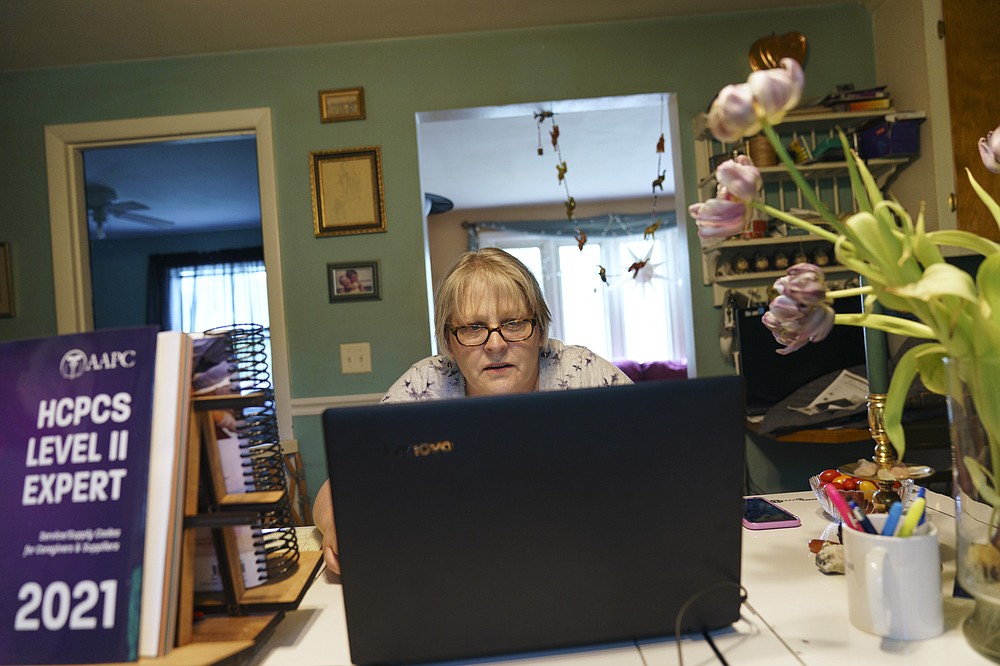 Ellen Booth, 57, studies at her kitchen table to become a certified medical coder, in Coventry, R.I., Monday, May 17, 2021. When the restaurant she worked for closed last year, Booth said it gave her "the kick I needed." She started a year-long class to learn to be a medical coder. When her unemployment benefits ran out two months ago, she started drawing on her retirement funds. Booth hopes to pass her upcoming exam and soon hit the job market. (AP Photo/David Goldman)