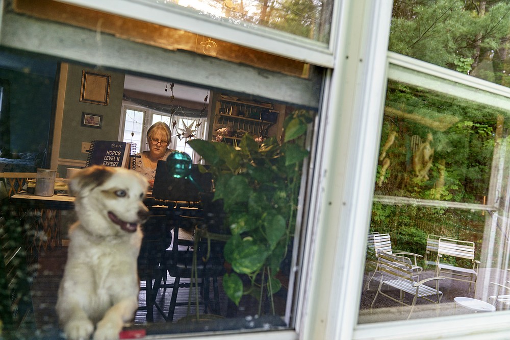 Ellen Booth, 57, studies at her kitchen table to become a certified medical coder as her dog, Rumble, looks out the window in Coventry, R.I., Monday, May 17, 2021. When the restaurant she worked for closed last year, Booth said it gave her "the kick I needed." She started a year-long class to learn to be a medical coder. When her unemployment benefits ran out two months ago, she started drawing on her retirement funds. Booth hopes to pass her upcoming exam and soon hit the job market. (AP Photo/David Goldman)