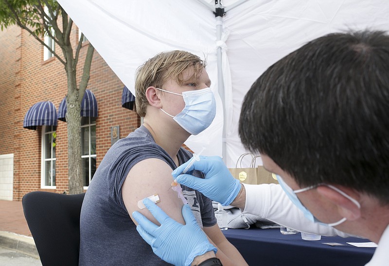 FILE -- Battalion Chief Justin Scantin (right) administers a covid-19 vaccine to Logan Redus, 17, Friday, May 7, 2021 at a pop-up clinic at the downtown square in Bentonville. (NWA Democrat-Gazette/Charlie Kaijo)